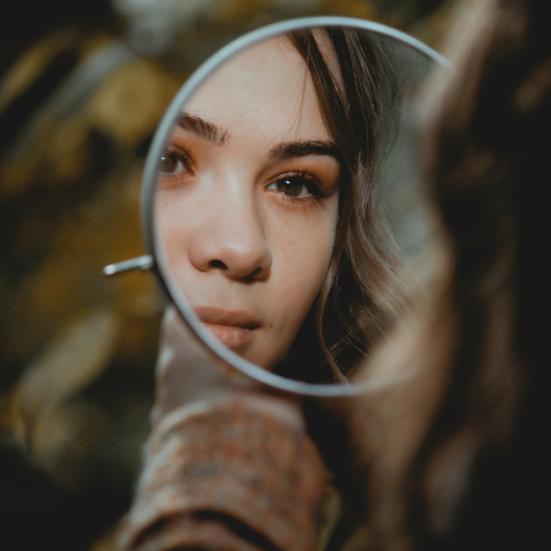 Ung kvinde betragter sit ansigt i et spejl.